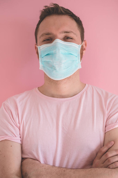 Ένας άντρας με μια ιογενή μάσκα σε ροζ φόντο, που φοράει προστασία προσώπου για την πρόληψη του ιού της στέψης. - Φωτογραφία, εικόνα