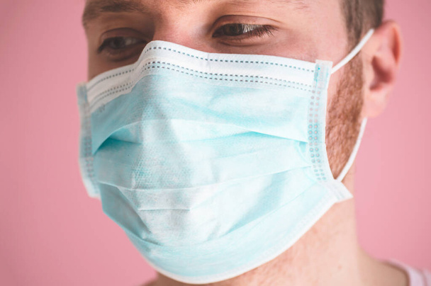 Een man met een viraal masker op een roze achtergrond, die gezichtsbescherming draagt ter voorkoming van coronavirus - Foto, afbeelding