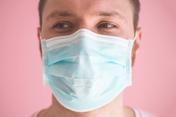 Ein Mann mit Virenmaske auf rosa Hintergrund, der einen Gesichtsschutz zur Vorbeugung gegen Coronavirus trägt - Foto, Bild