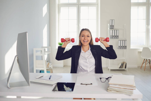 Businesswoman is doing exercises with dumbbells in the office during the break. - Fotografie, Obrázek