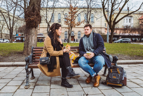 mladý dospělý pár Konzumujte rychlé občerstvení na lavičce městského parku. koncepce životního stylu - Fotografie, Obrázek