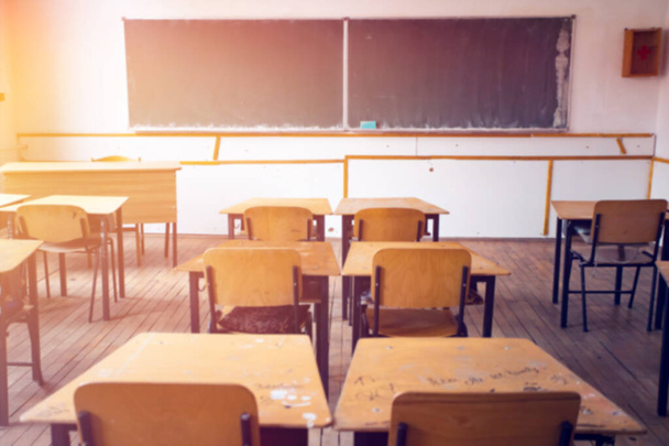 Back to school concept. Blurred view of sunny classroom with chairs, tables and blackboard. - 写真・画像
