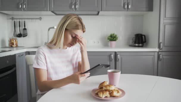 Sad woman using tablet device while having breakfast on her kitchen - Filmmaterial, Video