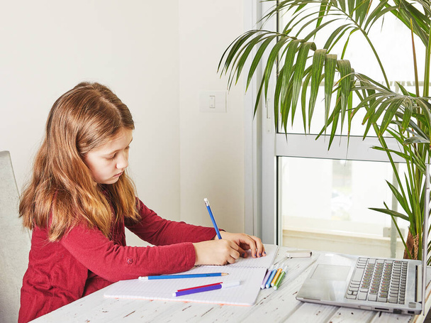 Enseignement à distance en ligne. Écolière étudiant à la maison avec un ordinateur portable et faisant des devoirs scolaires. Carnets de formation et stylos feutre colorés sur la table
 - Photo, image