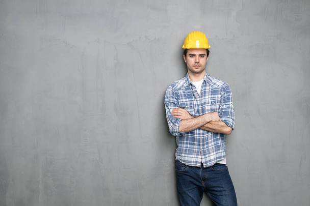 young worker standing against a concrete wall with safety helmet - Фото, изображение