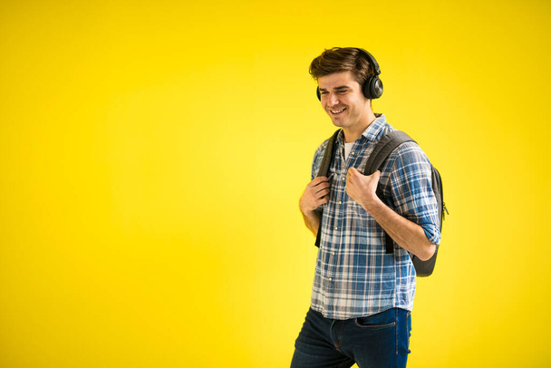 modern and cool young student listening music on the way to school on yellow background - 写真・画像