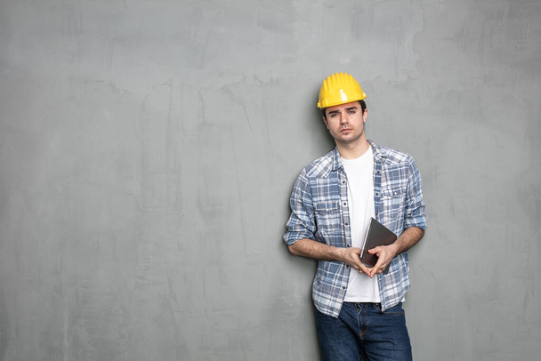 young engineer working and looking on a tablet for the project that he need to finish, standing on a industrial concrete wall - Фото, изображение