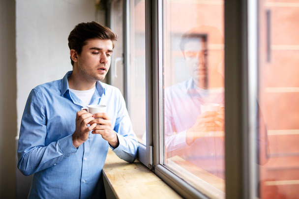 Isolated man standing next to a window in the safety of his own house - Photo, image