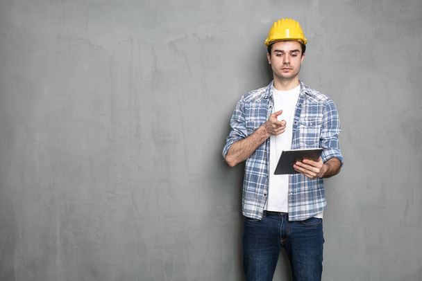 young engineer working and looking on a tablet for the project that he need to finish, standing on a industrial concrete wall - Foto, Imagem
