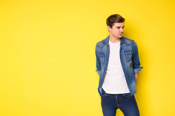 simple and cool guy in jeans looking to side, on yellow background - 写真・画像