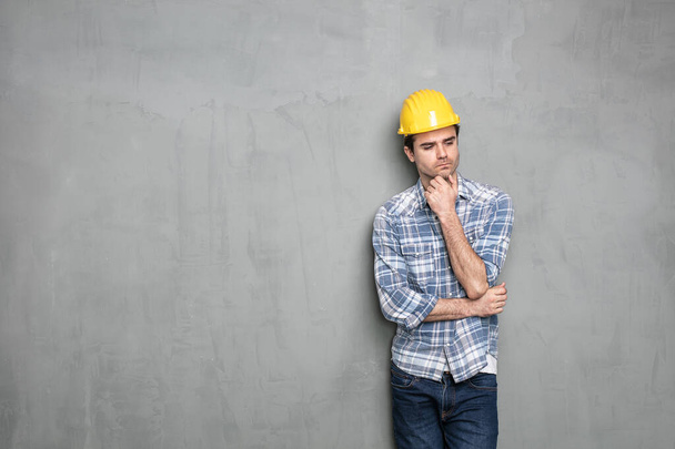 молодой рабочий, стоящий у бетонной стены с защитным шлемом
 - Фото, изображение