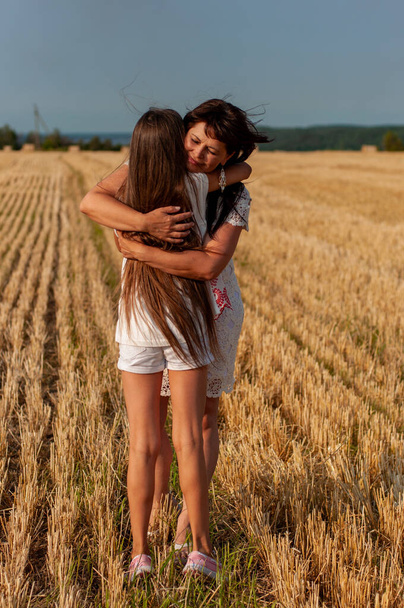 mooie vijftig-jarige vrouw knuffelt haar langharige dochter op de achtergrond van een tarweveld - Foto, afbeelding