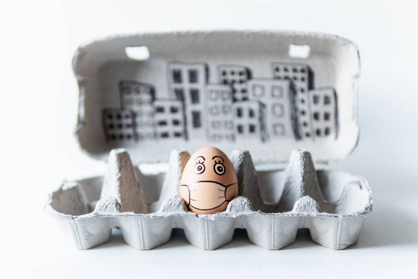 Kuřecí vejce v tácu s čmáranicí na obličeji v lékařské masce s panorama města na pozadí. Konceptuální obraz sociálního distancování a pobyt doma - Fotografie, Obrázek