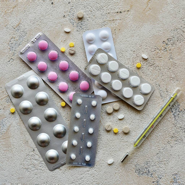 Termómetro y paquetes de pastillas sobre un fondo de piedra. Vista superior
. - Foto, Imagen