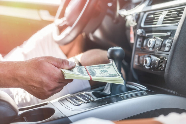 Car interior with male hand holding dollar bundle close up. Toned image - Photo, Image
