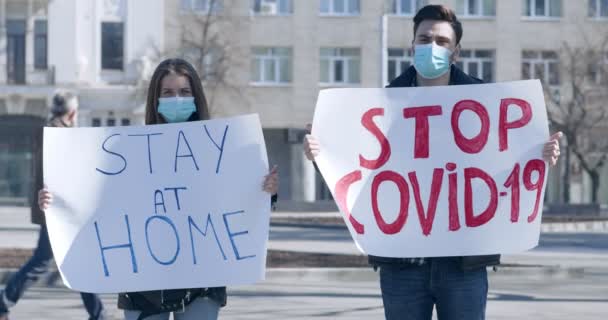 Jeune homme et jeune femme debout avec des pancartes RESTEZ À LA MAISON ET ARRETEZ COVID-19
 - Séquence, vidéo