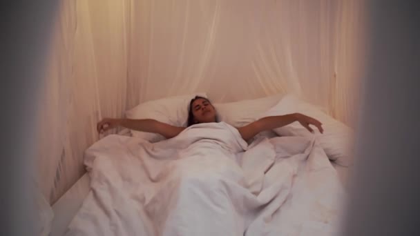 Schöne Brünette wacht am Morgen langsam auf, streckt sich und steht mit Baldachin aus dem Bett auf. Glückliches junges Mädchen begrüßt neuen Tag - Filmmaterial, Video