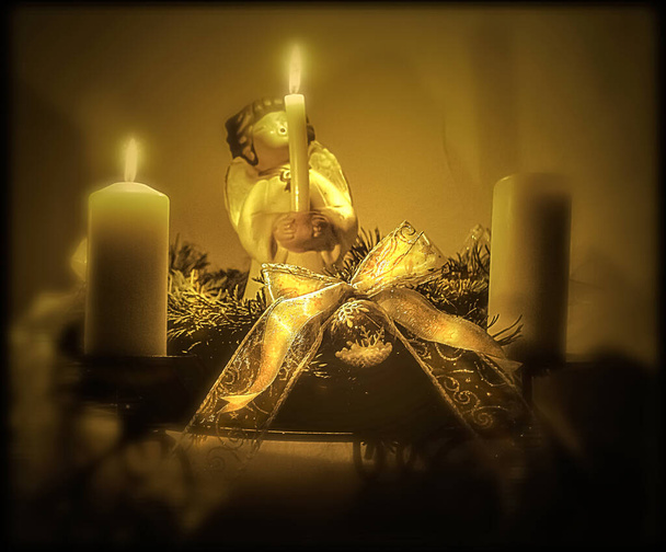 Χριστουγεννιάτικη διακόσμηση με πορσελάνινο άγγελο και αναμμένα κεριά σε χρυσαφί χρώμα με θολή, ατμοσφαιρική bokeh - Φωτογραφία, εικόνα