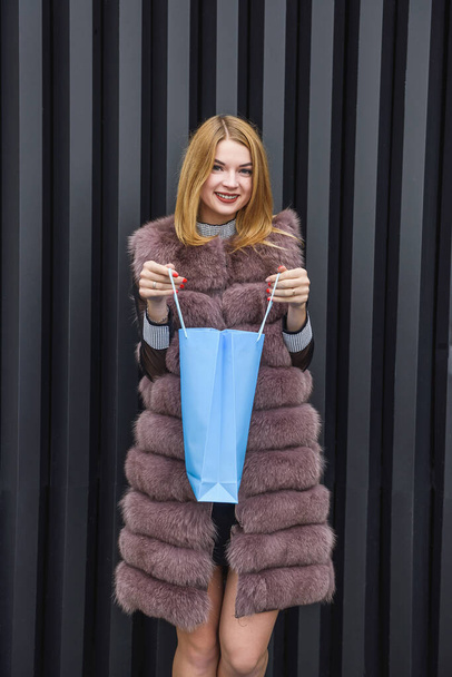 Mujer sorprendida con bolsa de compras en abrigo de piel posando al aire libre
 - Foto, Imagen