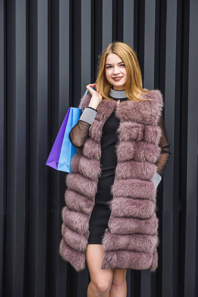 Urban portrait of young lady in fur coat. Woman in elegant dress posing on city street - Photo, Image