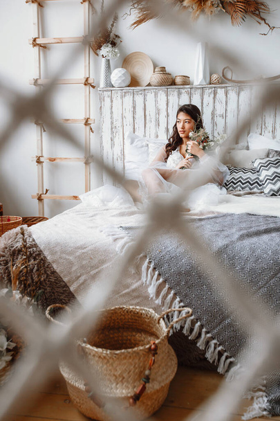 Ázsiai menyasszony fehérneműben, őszibarack a kezében, ül az ágyon - Fotó, kép