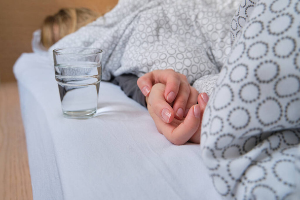 A glass of water next to a girl sleeping in bed. Happy morning. Woman in pajamas. Healthy lifestyle, wellness. Proper nutrition. Drinking water. Morning with water. Sunlight on linens. Pillow, blanket - Foto, Imagen