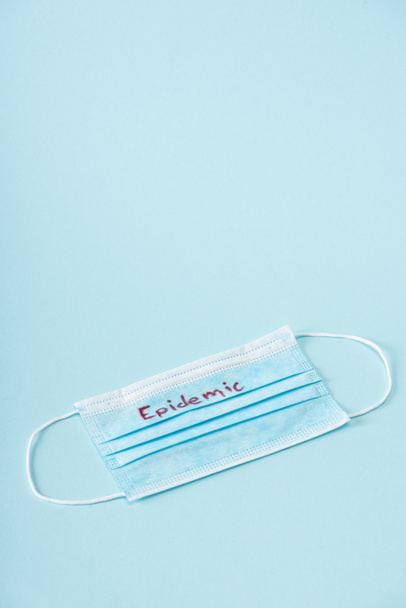 medical mask with epidemic lettering on blue with copy space - Fotoğraf, Görsel