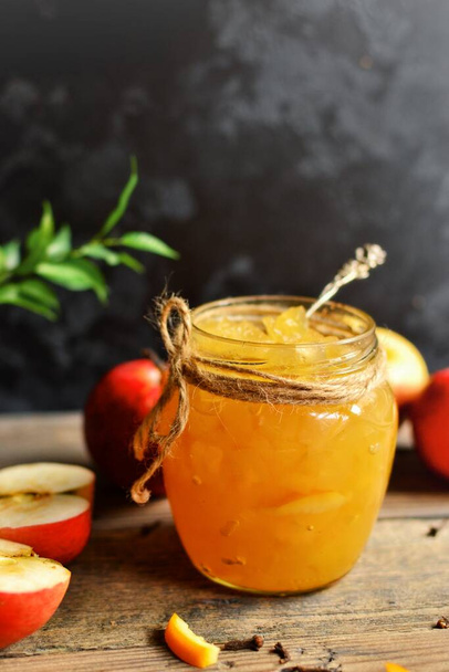 Σπιτική μαρμελάδα μήλο με ξύσμα πορτοκαλιού. Μαρμελάδα σε γυάλινο βάζο σε σκούρο φόντο, σε ξύλινο τραπέζι. - Φωτογραφία, εικόνα