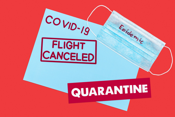 top view of blue envelope with covid-19, flight canceled and quarantine lettering near medical mask isolated on red  - 写真・画像