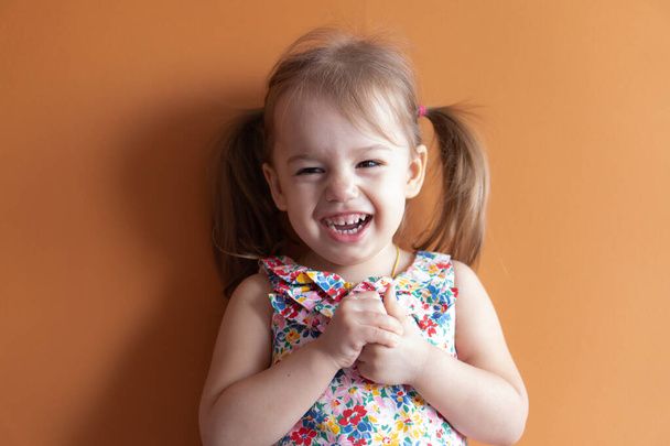 portrait of a beautiful little girl of two years on an orange background. Emotions of a young child - Photo, Image