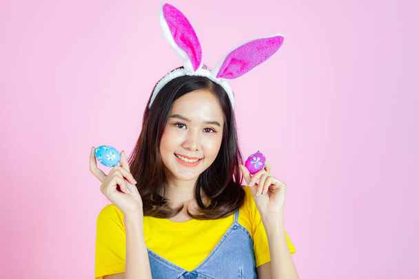 Portrait of a happy young woman wearing Easter bunny ears prepares to celebrate Easter on a pink background. - Fotoğraf, Görsel