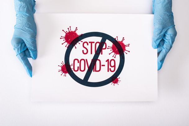 top view of doctor in latex gloves holding placard with stop covid-19 lettering on white  - Фото, изображение