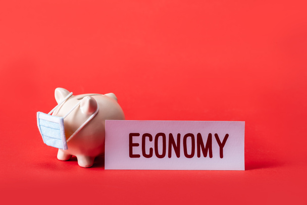 копилка в маленькой медицинской маске рядом с картой с экономичными надписями на красном
  - Фото, изображение