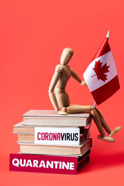 wooden doll with flag on canada books near cards with quarantine and coronavirus lettering on red  - Photo, Image