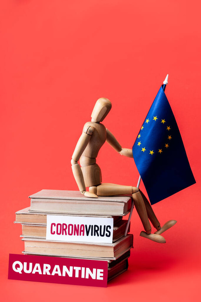 wooden doll with flag of european union on books near cards with quarantine and coronavirus lettering on red  - 写真・画像
