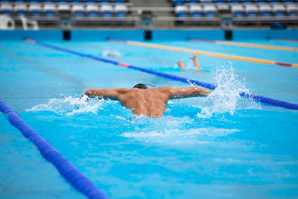 Homem atlético nadando em estilo borboleta na piscina com água azul clara
. - Foto, Imagem