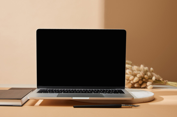 laptop with blank screen near lagurus spikelets, notebook and paintbrush on beige background - Foto, Imagem