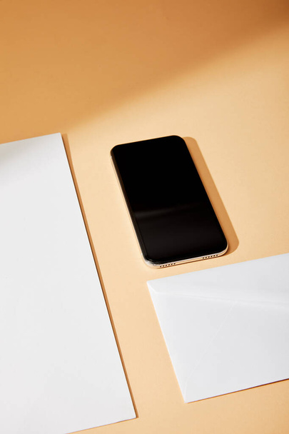 high angle view of smartphone near envelope and sheet of paper on beige background - Photo, Image