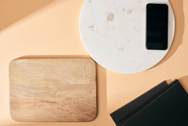 vrchní pohled na dřevěné a mramorové desky, smartphone a notebooky na béžovém pozadí - Fotografie, Obrázek