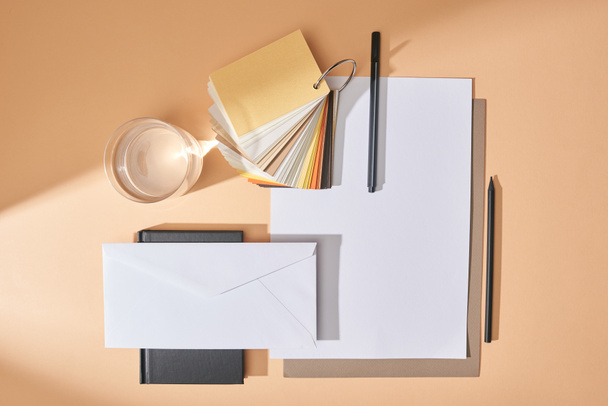 flat lay with glass of water, colors samples, sheets of paper, pens, envelope and notebook on beige background - Photo, image