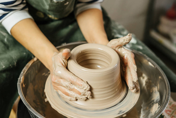 Hands of potter making clay pot on potter's wheel. Ceramics and pottery at the workshops.  - Foto, afbeelding