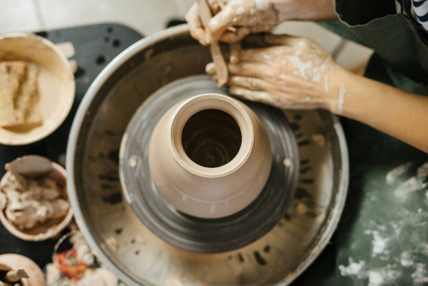 Hands of potter making clay pot on potter's wheel. Handmade pot at ceramic workshop. Pottery. Ceramic skills.  - Foto, afbeelding