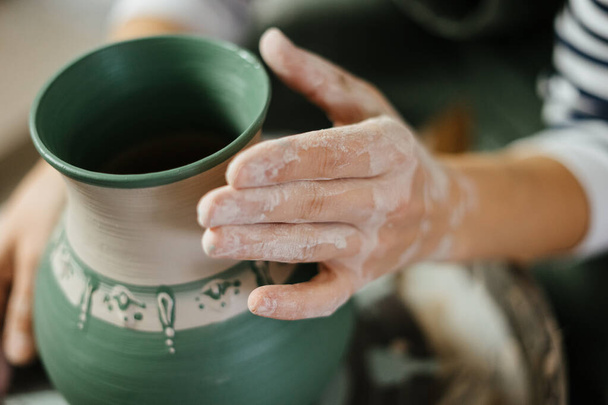 Die Hand des Künstlers neben dem bemalten handgefertigten Topf in der Keramikwerkstatt. Töpferei. Keramische Fertigkeiten.  - Foto, Bild