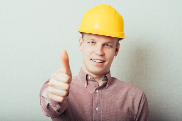 Construction worker in yellow hard hat. Happy male in his 20s. Young man portrait with thumbs up. - Φωτογραφία, εικόνα