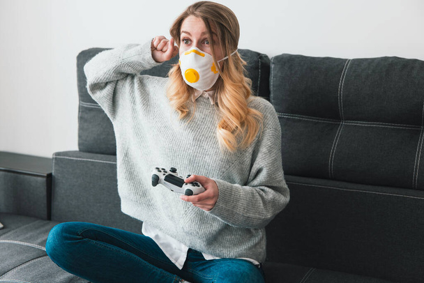 woman wearing medical protection mask playing online game with joystick in her hand clenching her fist in winning position isolated during quarantine, virus epidemic concept. - Fotó, kép