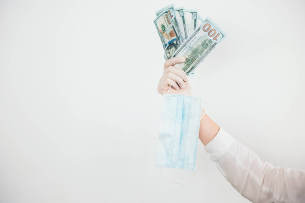 woman's hand in medical protection gloves holding cash and medical mask during Covid-19 epidemy on isolated white background, speculation concept. - Foto, afbeelding