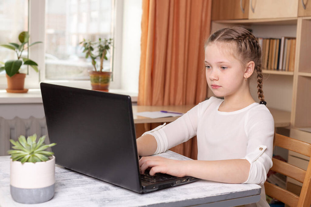 Serious schoolgirl working on a laptop. Distance learning online education, home school, home education, quarantine concept - Image - 写真・画像