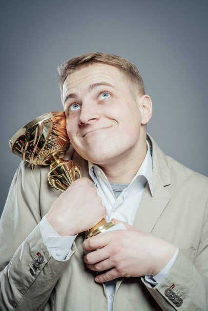 a winner with suit holding a cup/trophy over gray - Фото, зображення