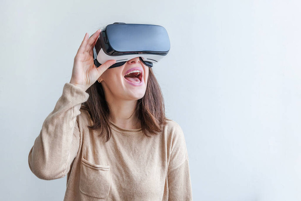 Smile young woman wearing using virtual reality VR glasses helmet headset on white background. Smartphone using with virtual reality goggles. Technology, simulation, hi-tech, videogame concept - Foto, Imagem