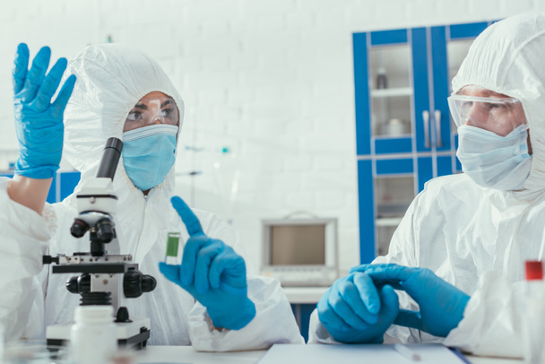 two biochemists in hazmat suits talking in laboratory near microscope - Photo, Image